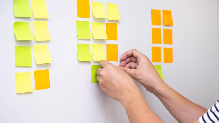 hands adding different coloured post-its to a wall